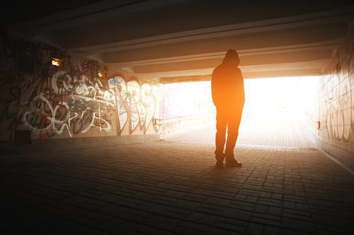 man in graffiti tunnel facing away toward sunset