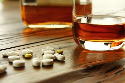 dangers-of-mixing-drugs-opiates-and-alcohol - whiskey or rum next to several pills