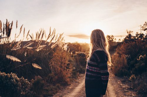 woman in sweater on nature path at sunset