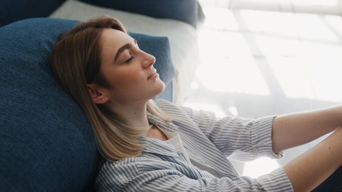 young woman laying on couch with her eyes closed - reduce stress