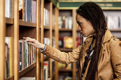 beautiful African American young woman browsing books at library or book store addiction self-help books