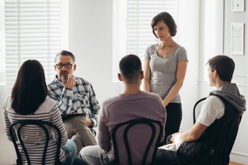family and facilitator holding an intervention - sitting in a circle in chairs and one person is standing to talk