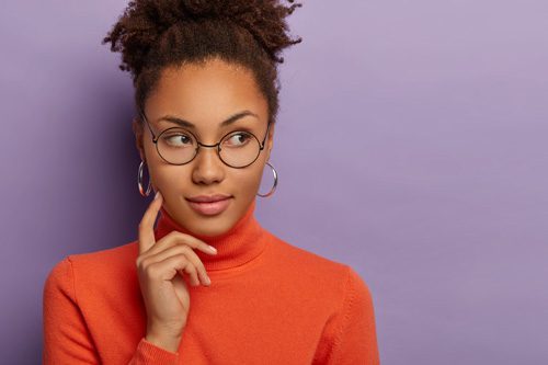 lovely Black young woman with glasses in an orange turtleneck sweater thinking - triggers